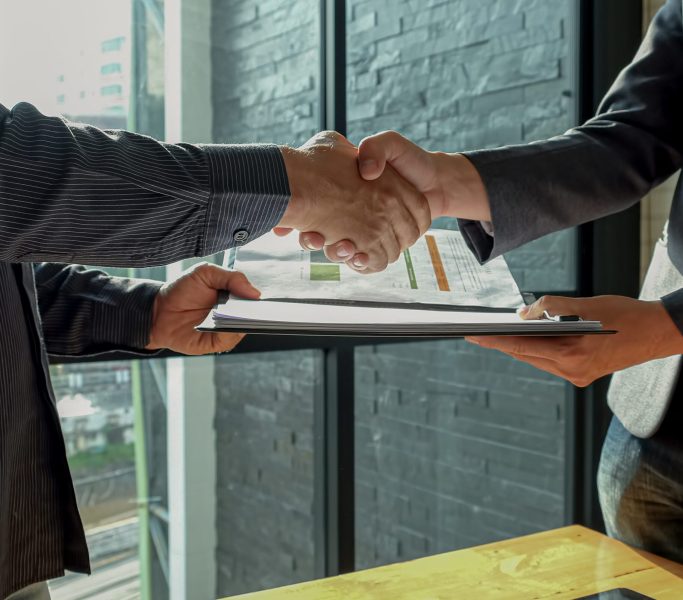 Businessman shakehand and exchanging contract documents.
