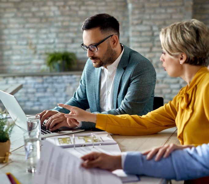 Financial advisor working on a computer while having a meeting with a couple in the office.